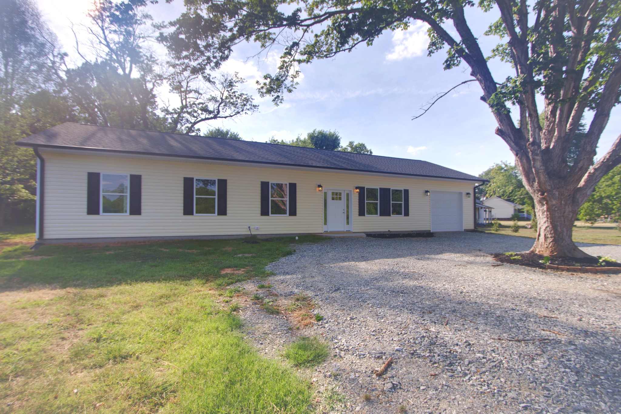 Front exterior of the single-story custom ranch home with gravel driveway and mature shade trees