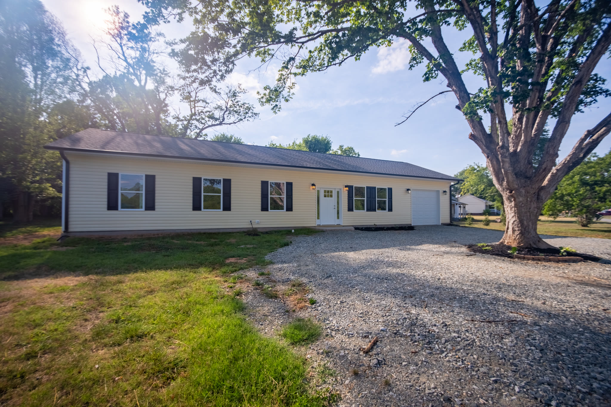 Front exterior of the single-story custom ranch home with gravel driveway and mature shade trees